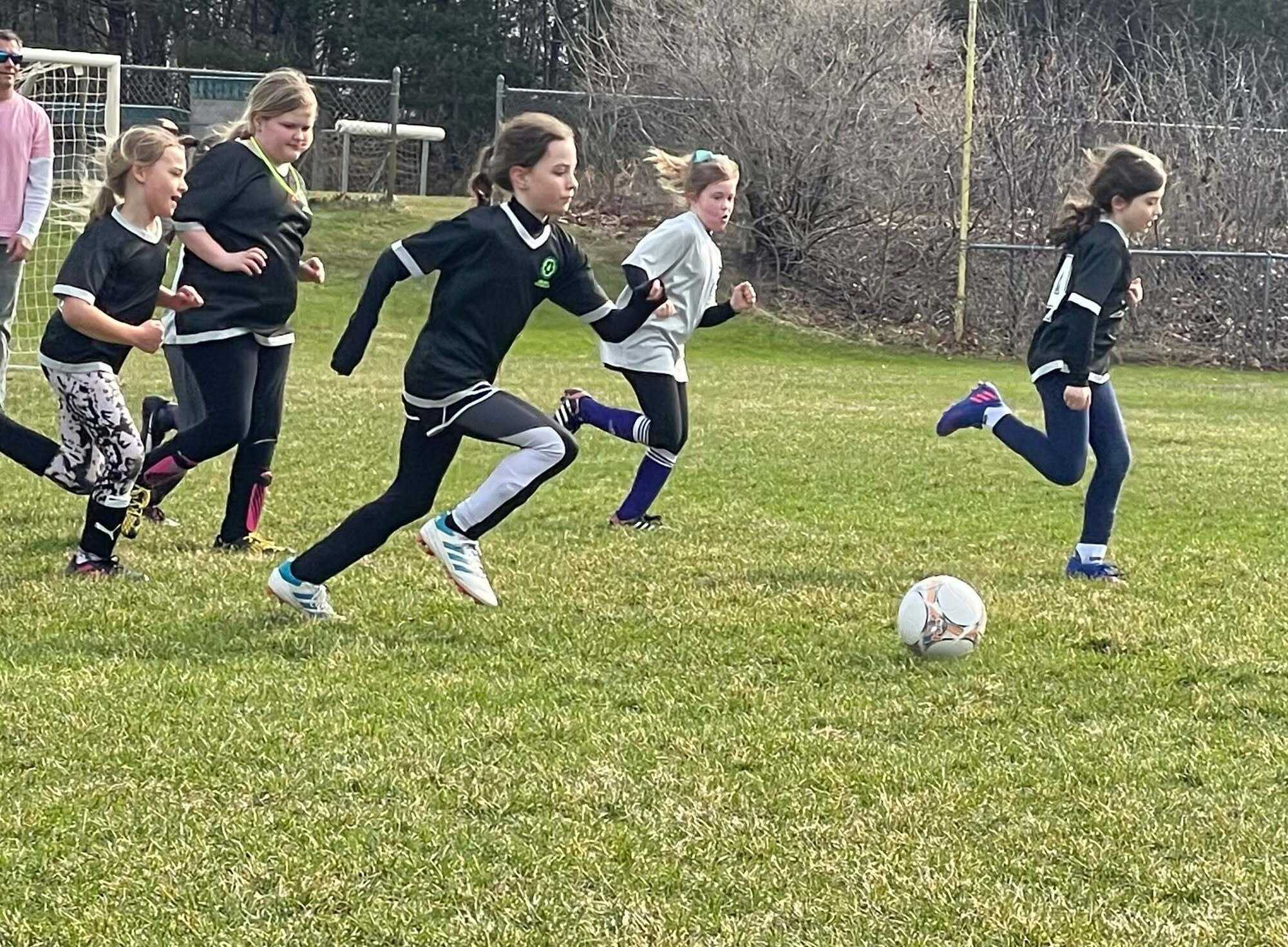 Girls in black and white shirts race each other for the ball